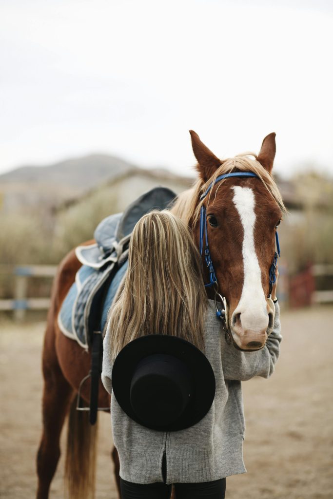 Eine Frau umarmt im Freien ein Pferd mit Sattel und demonstriert damit Freundschaft und Verbundenheit.